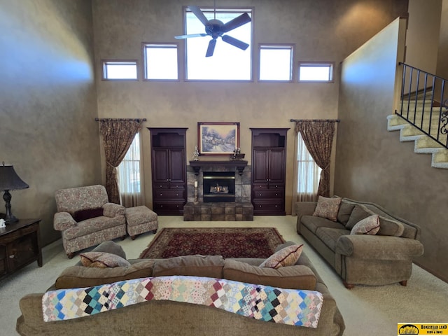 carpeted living room featuring a glass covered fireplace, ceiling fan, a high ceiling, and stairs