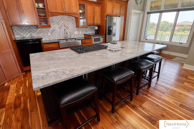 kitchen with stainless steel appliances, decorative backsplash, light wood-style floors, brown cabinetry, and a sink