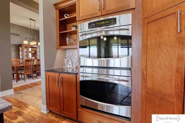 kitchen featuring brown cabinets, open shelves, visible vents, stainless steel double oven, and dark stone counters