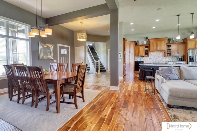 dining area with light wood-type flooring, beamed ceiling, stairway, and baseboards