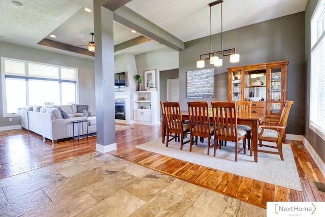 dining space with ceiling fan, a glass covered fireplace, wood finished floors, baseboards, and a raised ceiling