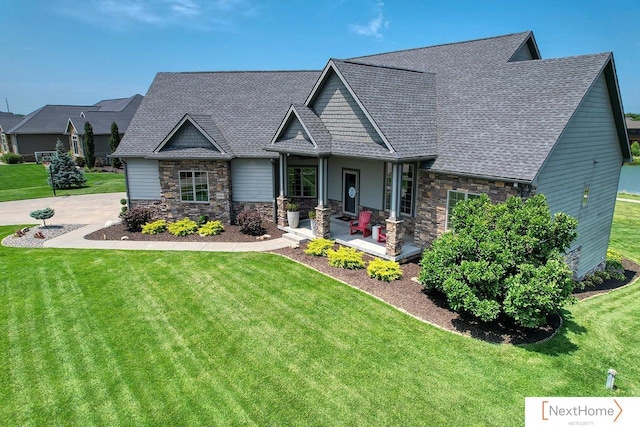 craftsman-style home with stone siding, a front yard, covered porch, and roof with shingles