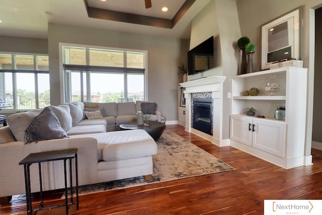 living area with a healthy amount of sunlight, a tray ceiling, dark wood finished floors, and a tile fireplace