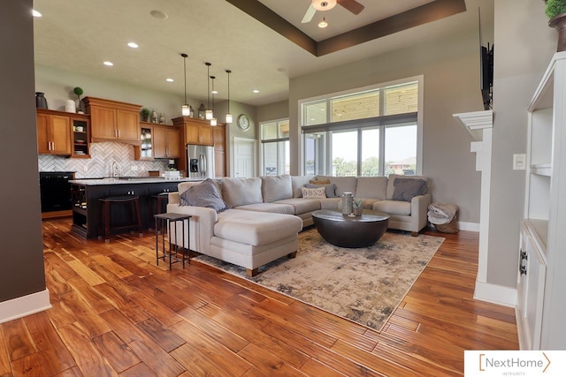 living area with recessed lighting, wood finished floors, a ceiling fan, a towering ceiling, and baseboards