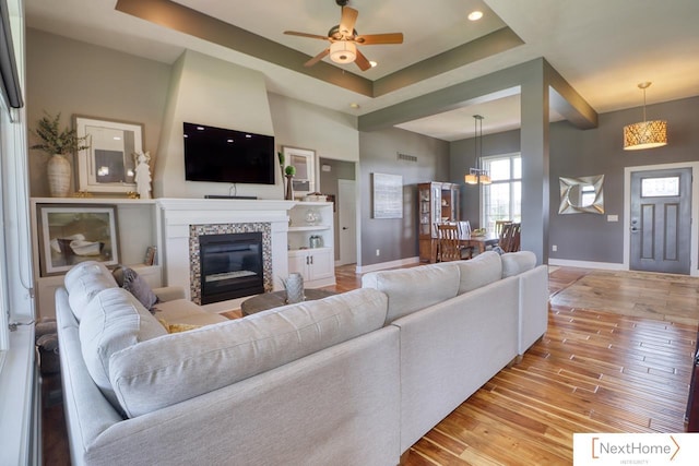 living area with a tray ceiling, light wood finished floors, a tiled fireplace, and baseboards