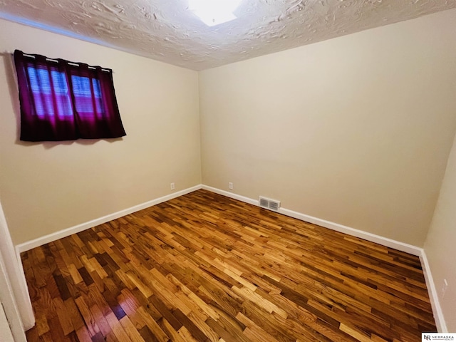 empty room with visible vents, a textured ceiling, baseboards, and wood finished floors