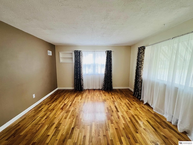 spare room with a textured ceiling, wood finished floors, visible vents, and baseboards