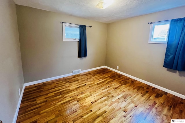 empty room featuring visible vents, plenty of natural light, baseboards, and wood finished floors