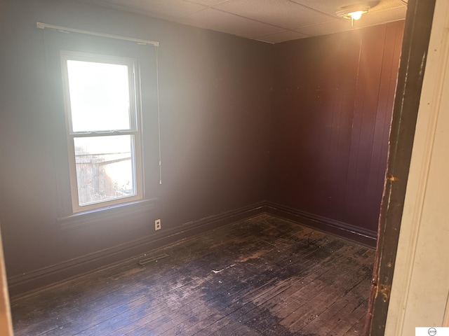 spare room with a drop ceiling, dark wood finished floors, and baseboards