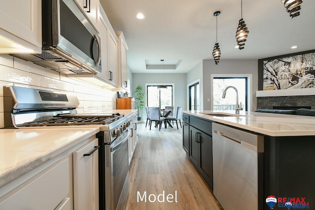 kitchen featuring stainless steel appliances, tasteful backsplash, light wood-style floors, white cabinetry, and a sink