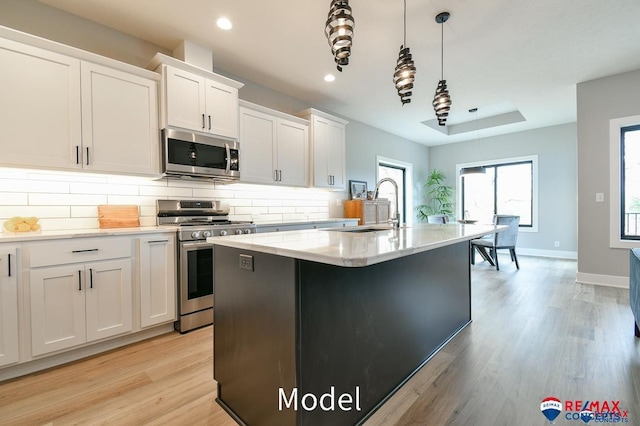 kitchen featuring light wood finished floors, decorative backsplash, stainless steel appliances, white cabinetry, and a sink