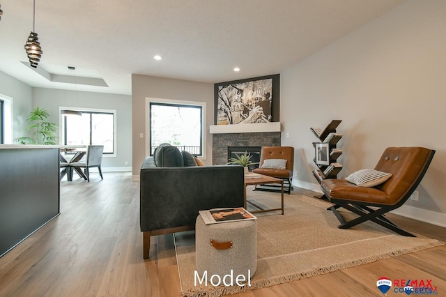 living area featuring a raised ceiling, a fireplace, wood finished floors, and baseboards