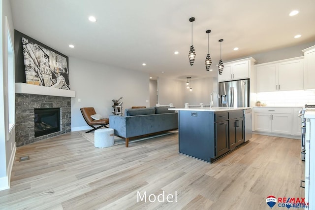 kitchen with a stone fireplace, white cabinetry, open floor plan, appliances with stainless steel finishes, and light wood-type flooring