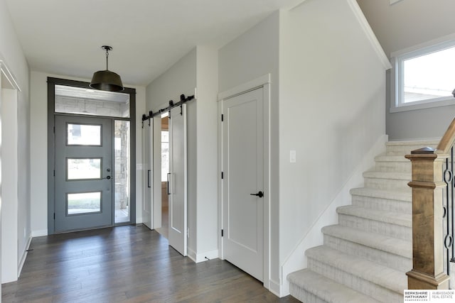 foyer entrance featuring a barn door, dark wood-style flooring, stairway, and baseboards