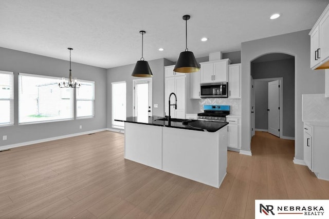 kitchen with stainless steel appliances, a sink, white cabinets, light wood-type flooring, and backsplash