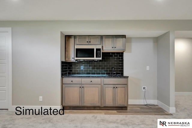 kitchen featuring light carpet, a sink, baseboards, tasteful backsplash, and stainless steel microwave