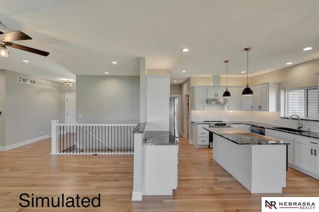 kitchen featuring visible vents, dark stone counters, a center island, light wood-type flooring, and a sink