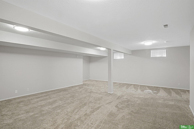 below grade area featuring carpet floors, baseboards, visible vents, and a textured ceiling