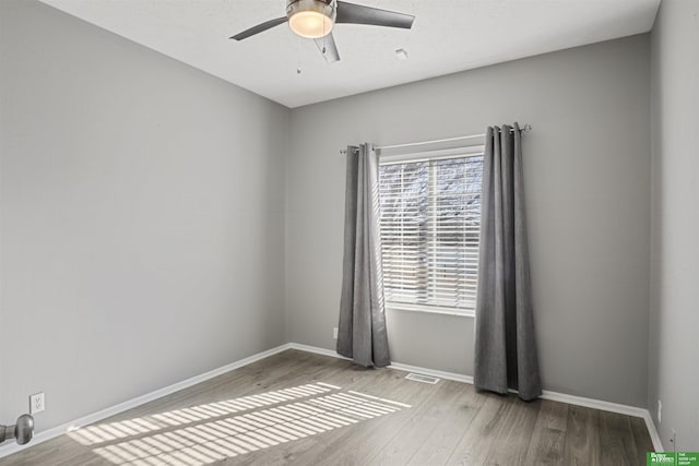 empty room with a ceiling fan, visible vents, baseboards, and wood finished floors