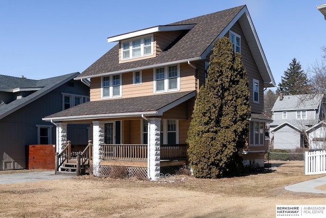 american foursquare style home with a shingled roof, covered porch, and fence