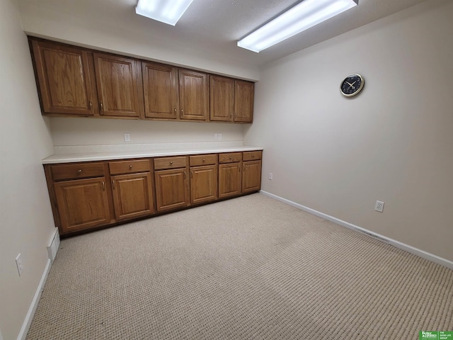 interior space with visible vents, baseboards, brown cabinetry, light colored carpet, and light countertops