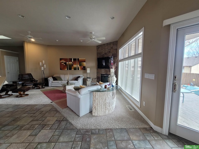 living area with baseboards, visible vents, a ceiling fan, stone finish flooring, and a fireplace