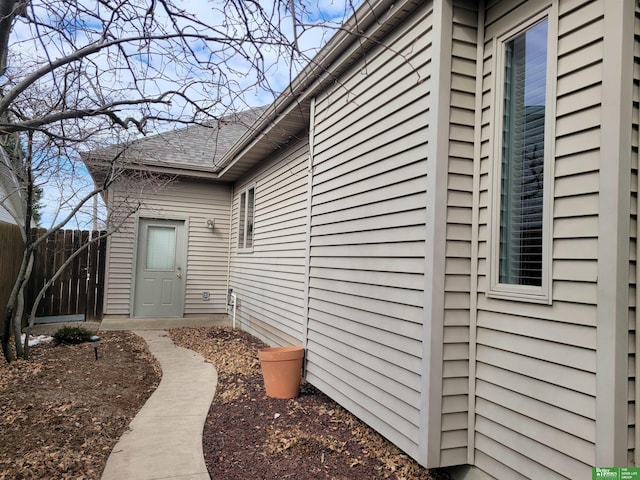 view of exterior entry with a shingled roof and fence