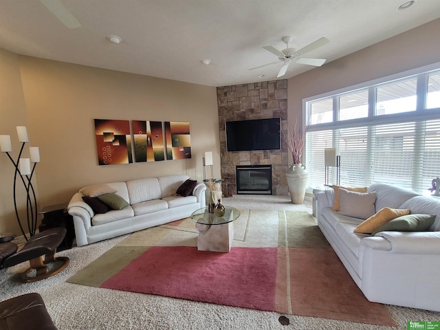 living room featuring carpet floors, ceiling fan, and a stone fireplace