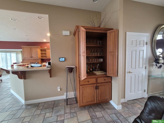 kitchen with a breakfast bar area, open shelves, recessed lighting, stone finish floor, and baseboards