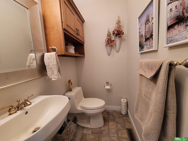 half bathroom with toilet, visible vents, baseboards, and a sink