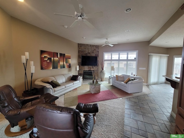 living room featuring stone tile floors, a fireplace, ceiling fan, and a wealth of natural light