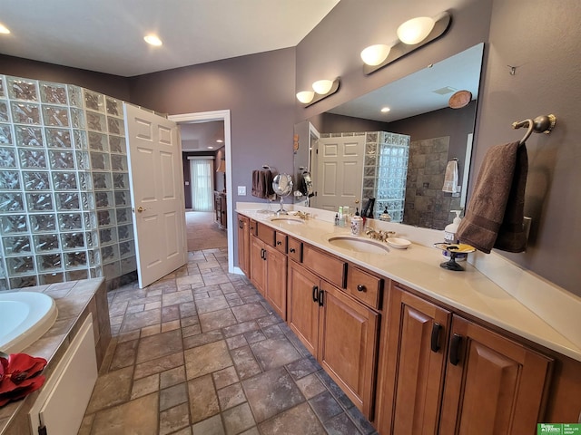 bathroom featuring stone tile floors, double vanity, a sink, a walk in shower, and a bath