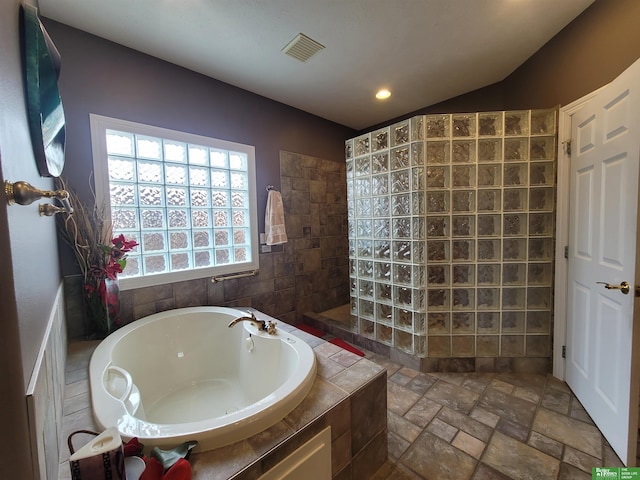 full bath with stone tile flooring, visible vents, vaulted ceiling, a bath, and walk in shower