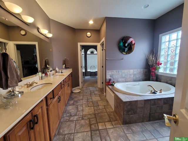 bathroom featuring stone tile flooring, a garden tub, double vanity, and a sink