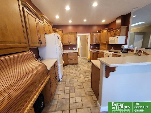 kitchen featuring stone tile floors, recessed lighting, white appliances, a peninsula, and a kitchen breakfast bar