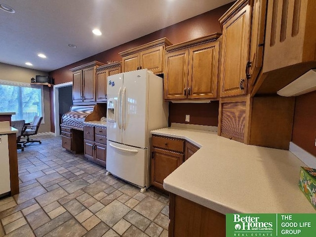 kitchen featuring recessed lighting, stone tile floors, light countertops, brown cabinets, and white fridge with ice dispenser