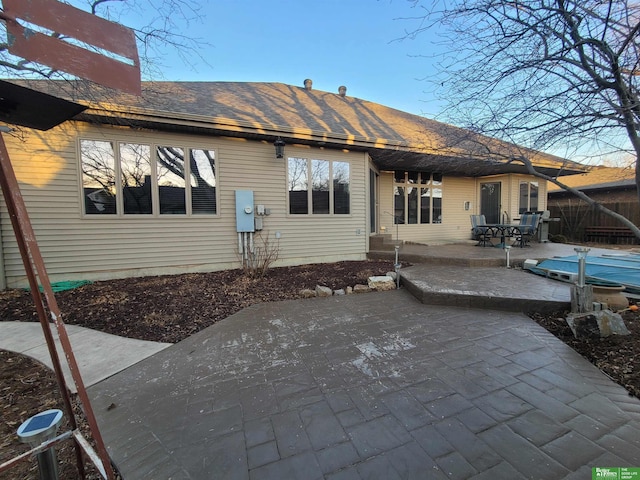 rear view of house featuring a shingled roof, a patio area, fence, and a covered pool