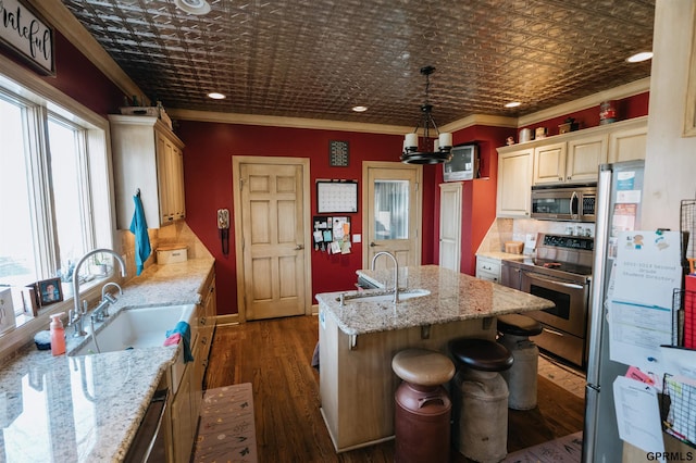 kitchen with an ornate ceiling, appliances with stainless steel finishes, ornamental molding, a kitchen island with sink, and a sink