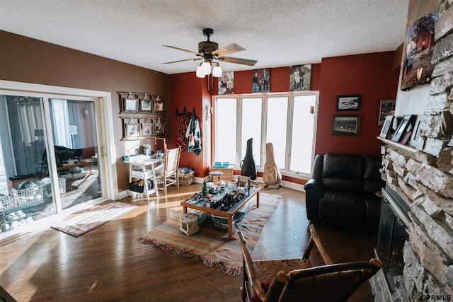 living area with a textured ceiling, ceiling fan, a fireplace, wood finished floors, and baseboards