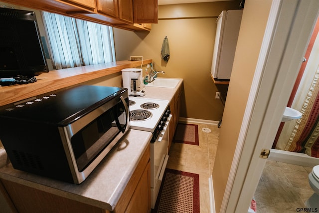 kitchen featuring white electric range, a sink, baseboards, brown cabinets, and stainless steel microwave