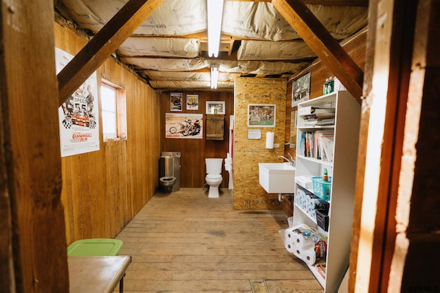 interior space with wood-type flooring, a sink, wooden walls, and toilet