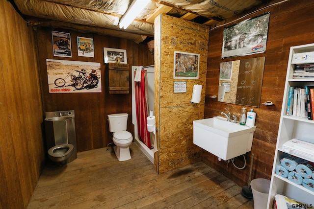 bathroom with wooden walls, toilet, hardwood / wood-style flooring, curtained shower, and a sink