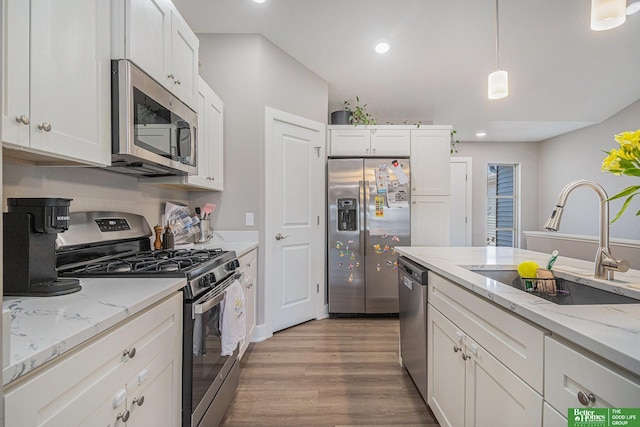 kitchen with wood finished floors, a sink, white cabinets, appliances with stainless steel finishes, and decorative light fixtures