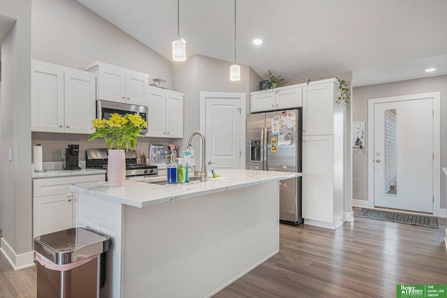 kitchen featuring lofted ceiling, wood finished floors, hanging light fixtures, stainless steel appliances, and white cabinetry