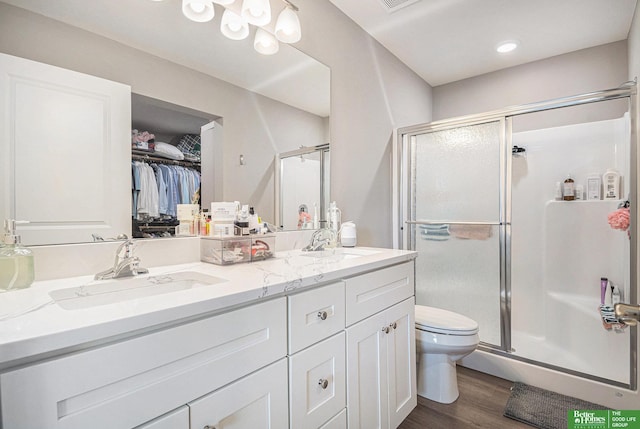 bathroom featuring double vanity, wood finished floors, a stall shower, and a sink