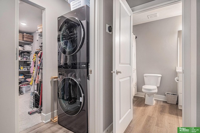 interior space featuring laundry area, stacked washer / dryer, wood finished floors, visible vents, and baseboards