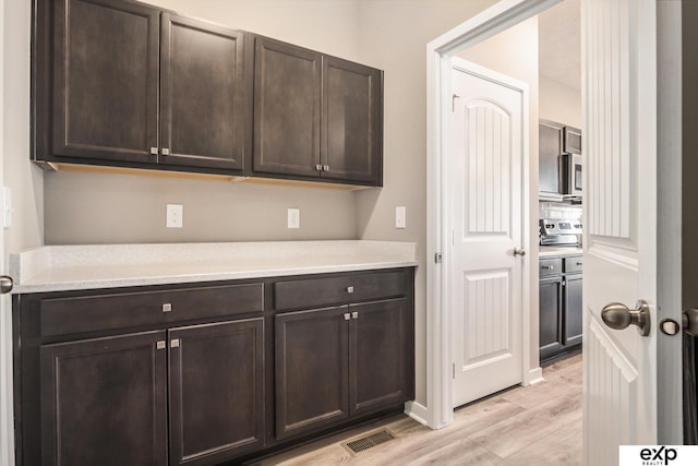 kitchen featuring dark brown cabinetry, stainless steel appliances, visible vents, light countertops, and light wood finished floors