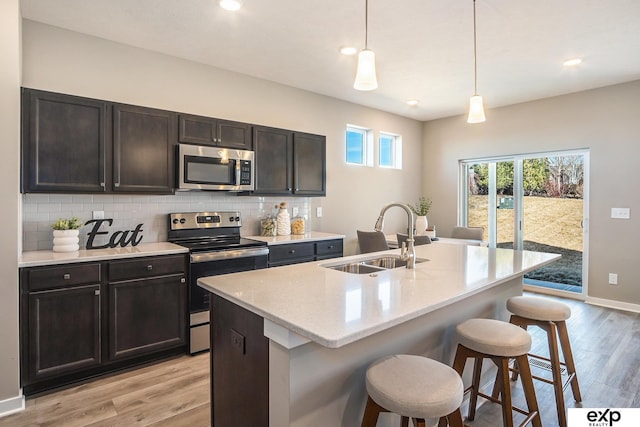 kitchen with a sink, a kitchen breakfast bar, light wood-style floors, appliances with stainless steel finishes, and tasteful backsplash