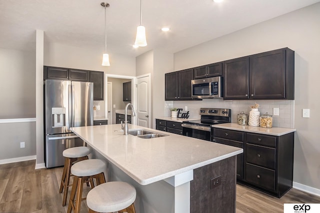 kitchen with light wood finished floors, decorative backsplash, appliances with stainless steel finishes, a sink, and a kitchen bar