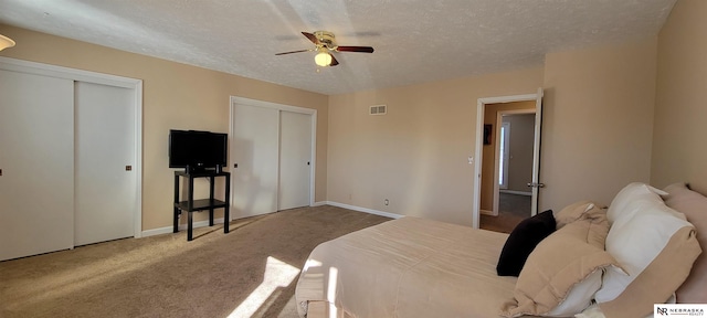 bedroom featuring a textured ceiling, a ceiling fan, visible vents, multiple closets, and carpet